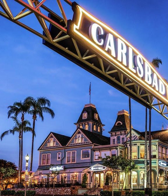 Historic building under Carlsbad sign at dusk with palm trees.