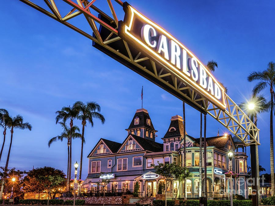 Historic building under Carlsbad sign at dusk with palm trees.