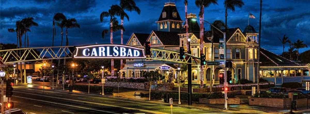 Night view of Carlsbad sign and lit-up building with palm trees.