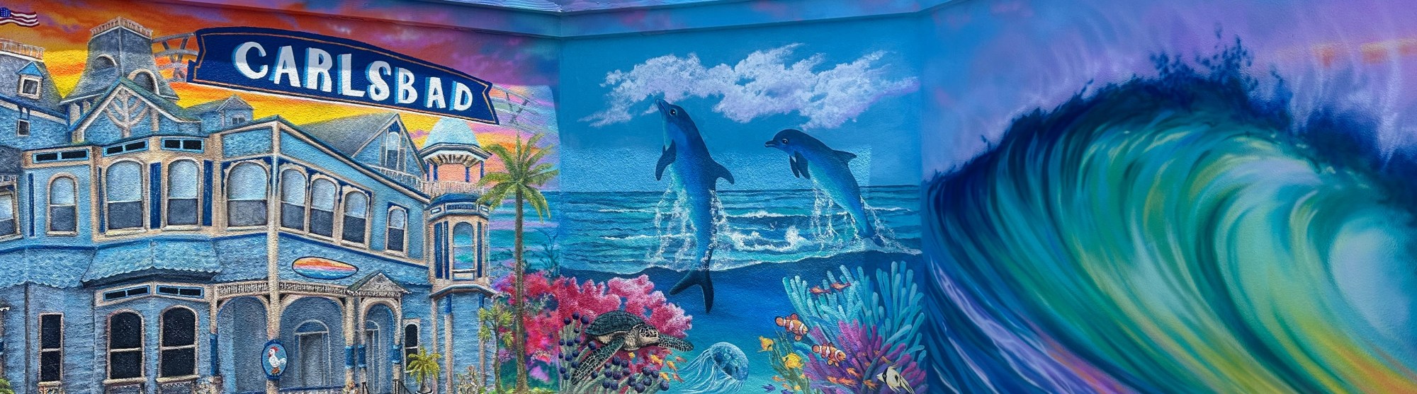 Colorful mural with dolphins, wave, house, coral, and 'Carlsbad' sign.