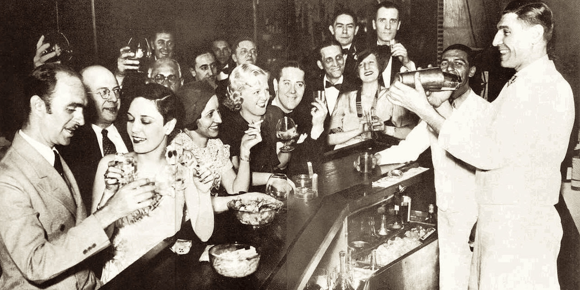 Group of people at a bar celebrating, with a bartender shaking a cocktail.
