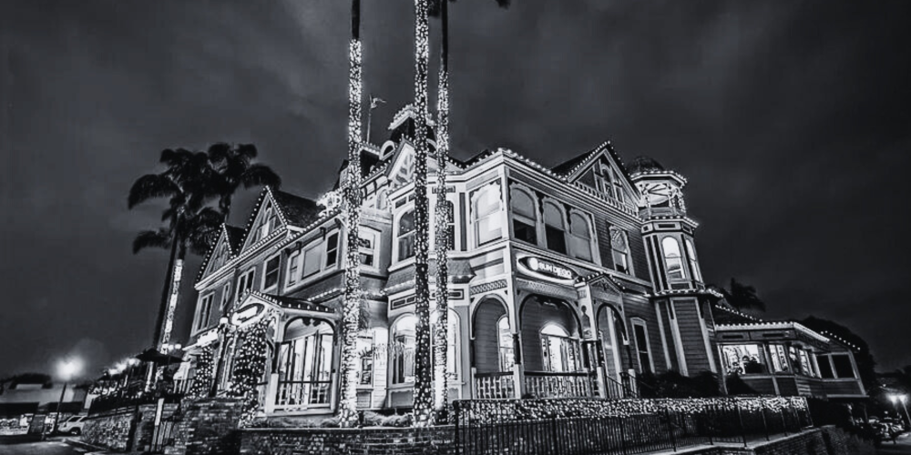 Black and white photo of a large Victorian-style house with decorative lights at night.