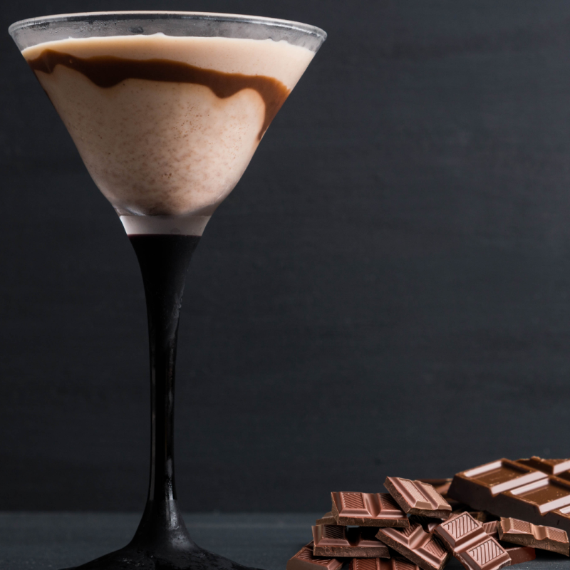 Martini glass with chocolate cocktail and chocolate pieces on a dark surface.