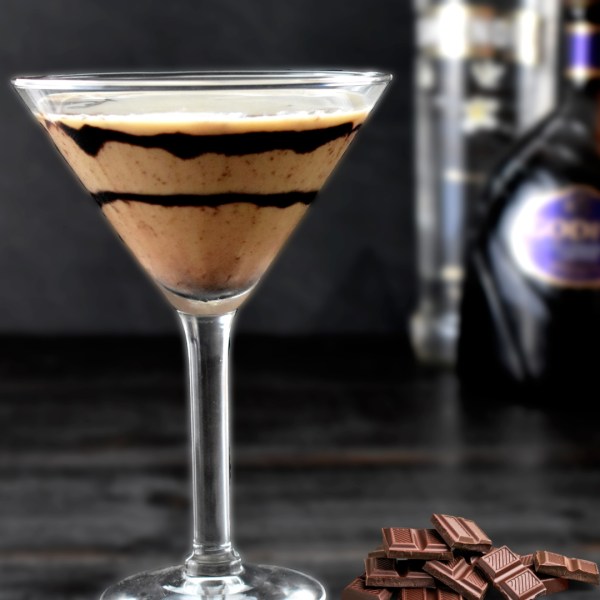 Martini glass with layered chocolate cocktail, bottles, and chocolate pieces nearby.