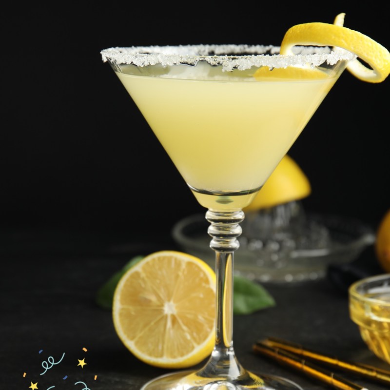 Bee's Knee's Cocktail A lemon cocktail in a glass with sugar rim and lemon twist, surrounded by lemon halves.