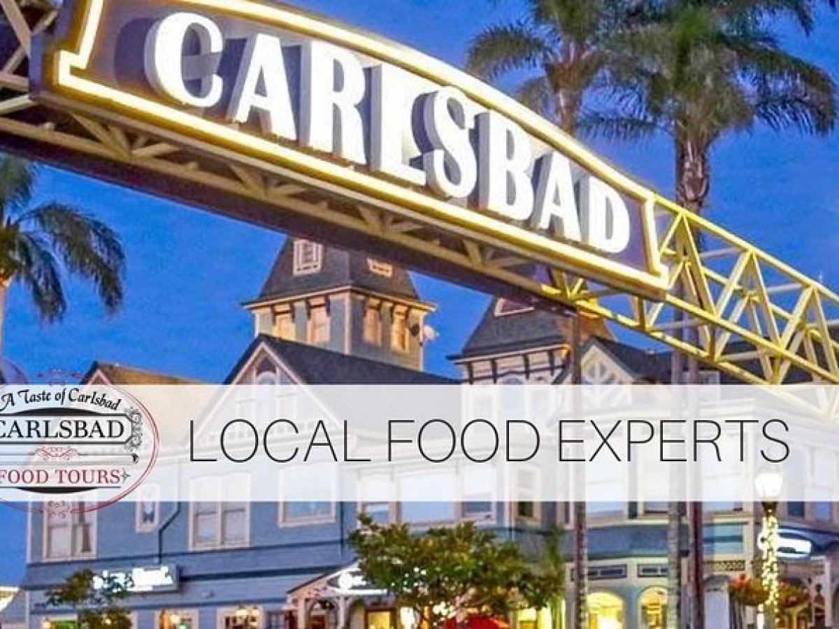 Carlsbad sign over street with shops and palm trees at dusk.