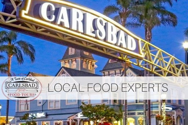 Carlsbad sign over street with shops and palm trees at dusk.
