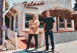 Two men standing in front of a restaurant with a sign and thatched roof.