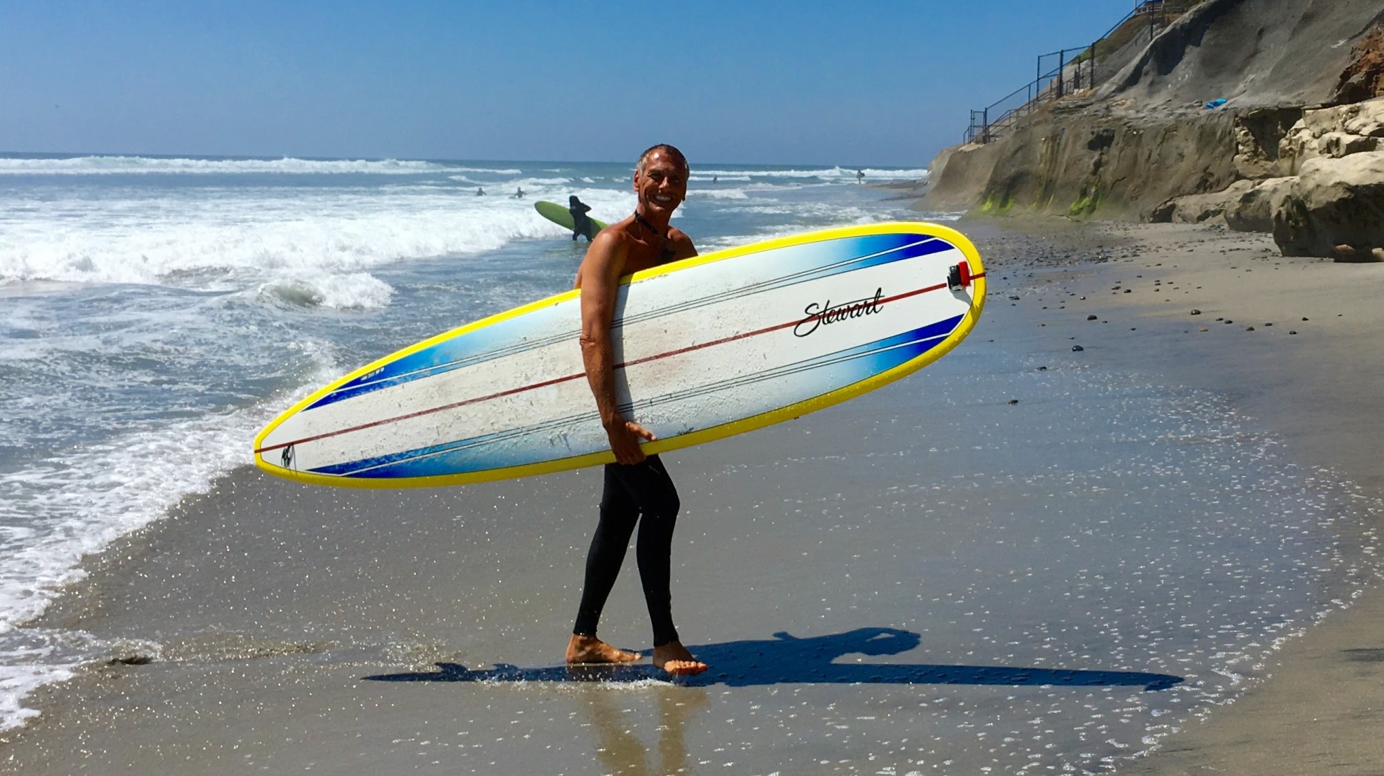 Person holding a surfboard on a sandy beach with ocean waves in the background.