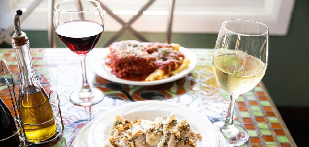 Table with red and white wine, pasta, and olive oil in bottles.