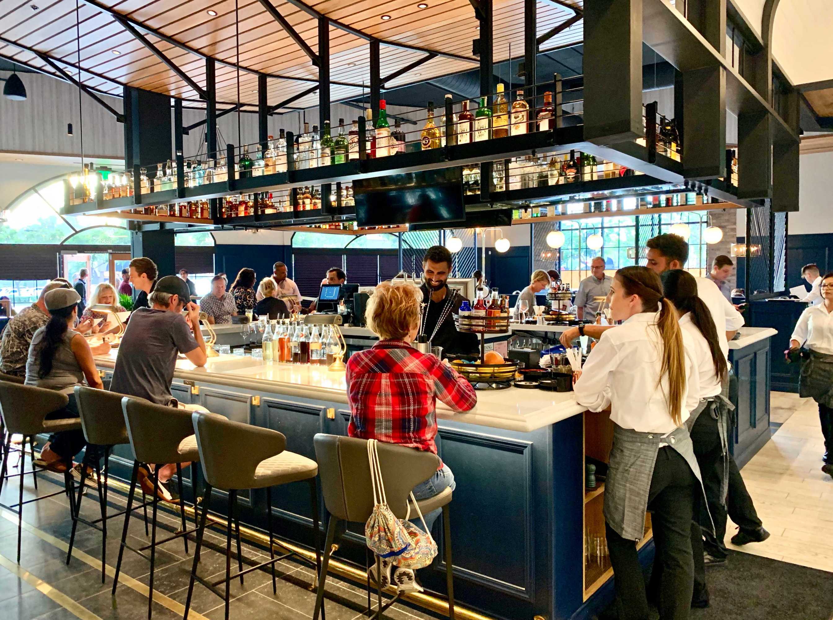 People sitting at a bar with bottles on shelves above and staff serving.