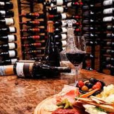 Wine cellar with bottles on shelves, a wine glass, and a meat and cheese platter on a wooden table.