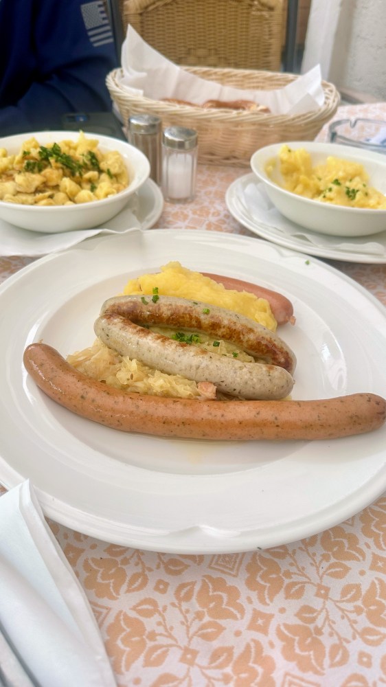 Three sausages on sauerkraut with mashed potatoes, side dishes on table.