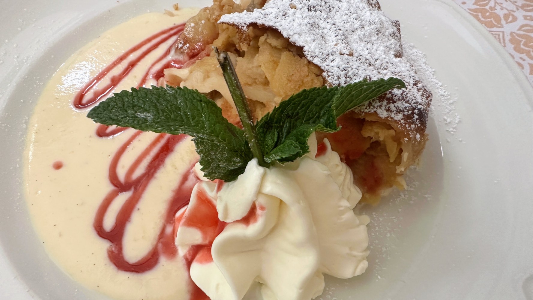 Apple strudel with whipped cream, mint, custard, and berry sauce.