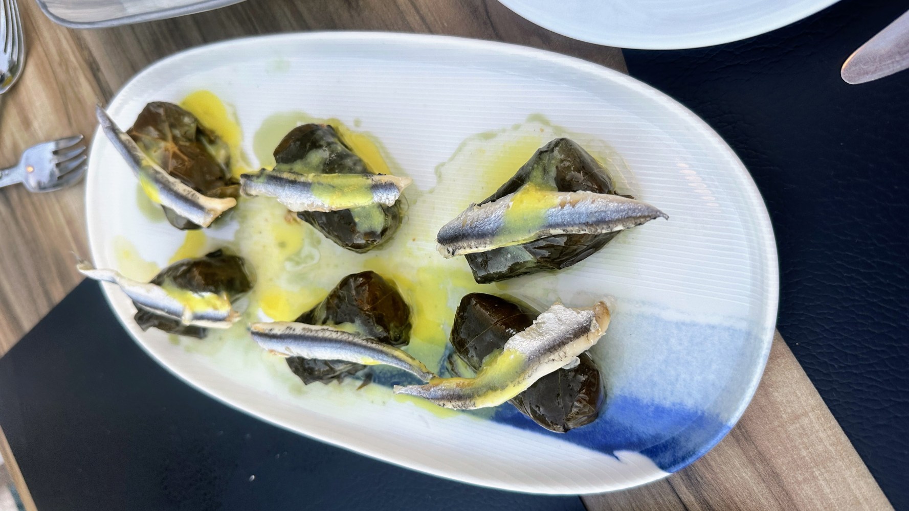 Stuffed grape leaves topped with anchovies on a white oval plate.