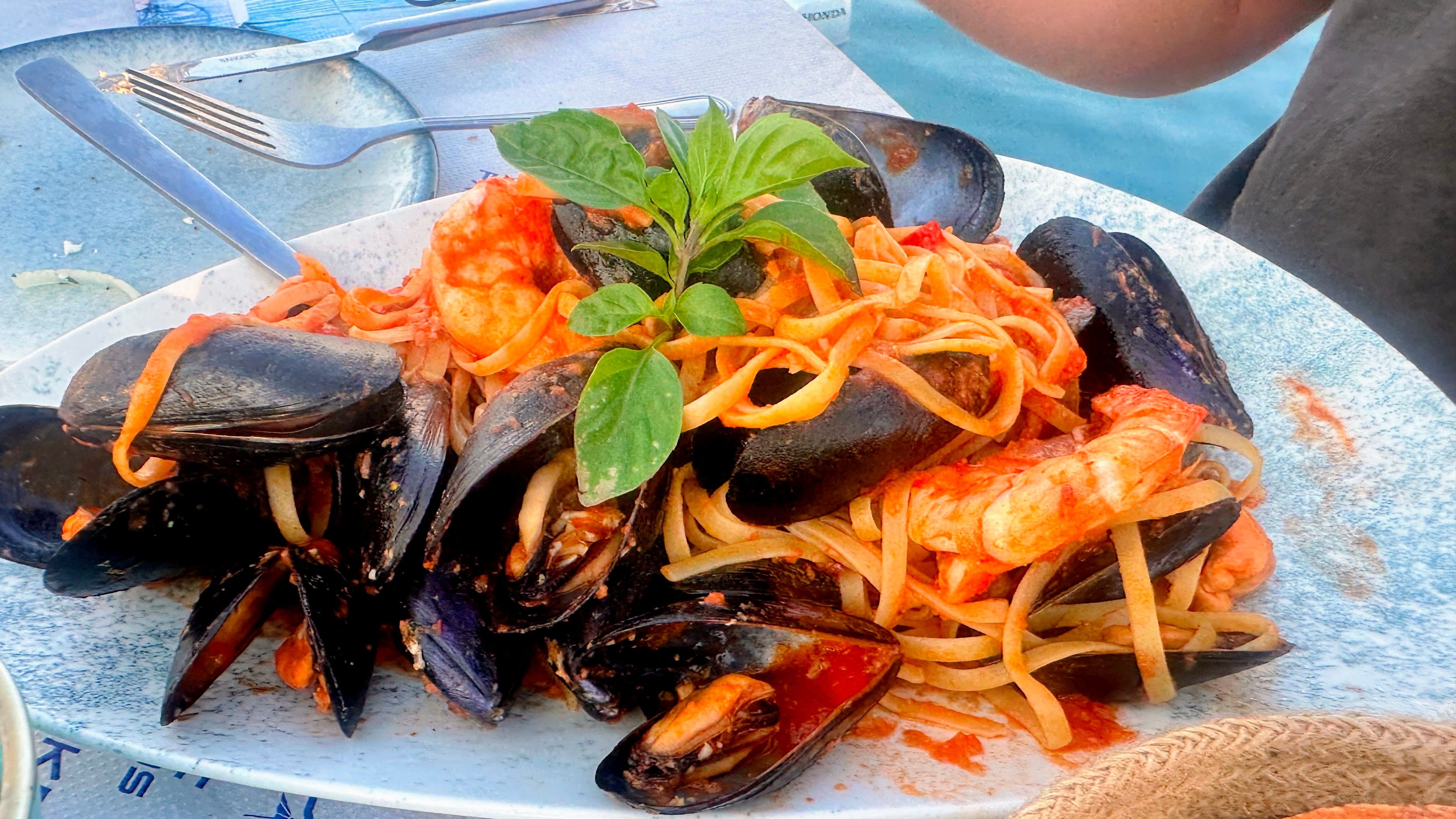 Seafood pasta with mussels, shrimp, and basil on a white plate.
