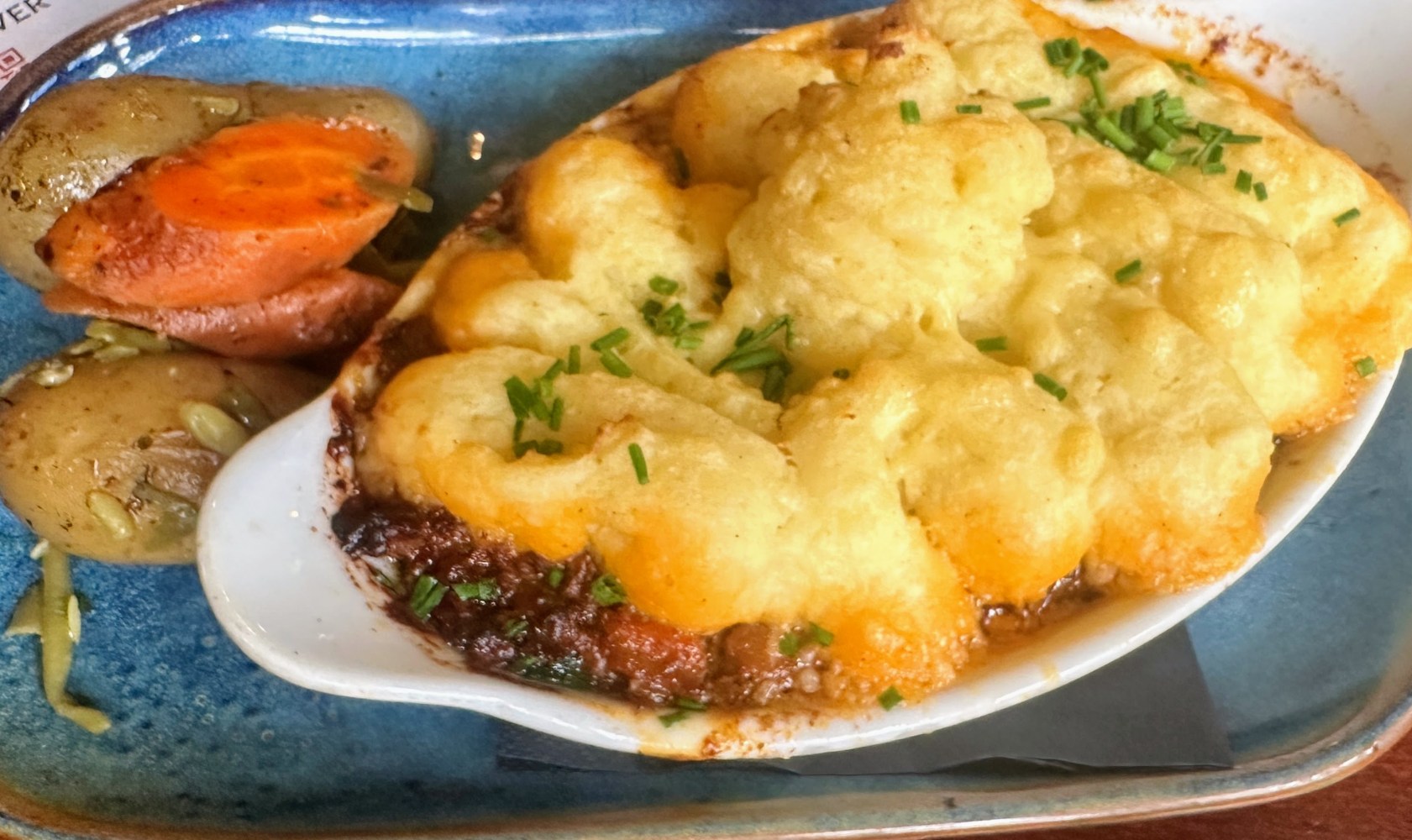 Baked dish with mashed potato topping and chives beside roasted vegetables on a blue plate.