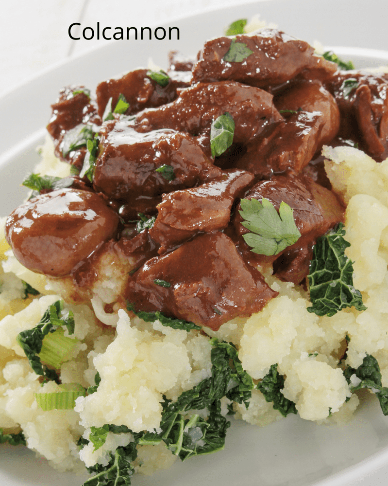 Colcannon topped with beef stew and parsley on a white plate.