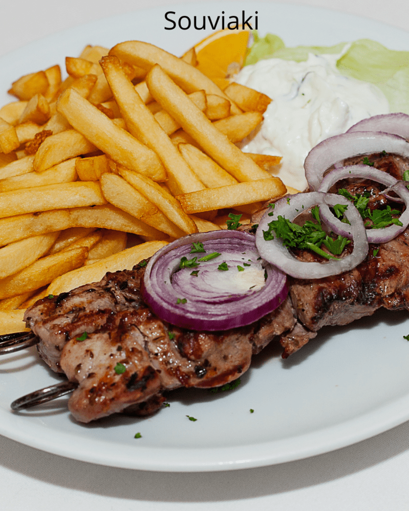Plate with souvlaki skewers, fries, onion slices, parsley, and sauce.