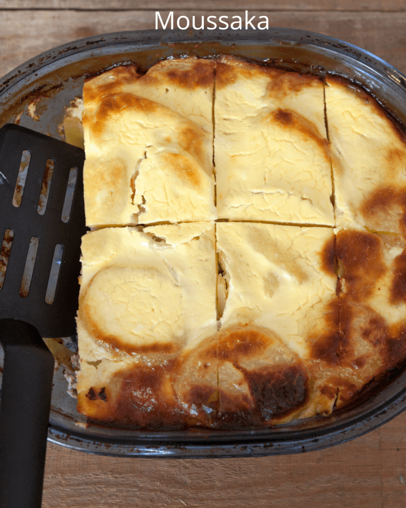 Moussaka dish in a tray, cut into six pieces with a spatula on the side.