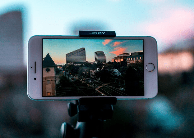 Smartphone on tripod capturing cityscape with buildings at sunset.