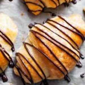 Three croissants drizzled with chocolate on parchment paper.