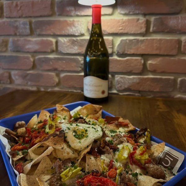Plate of loaded nachos with a bottle of wine and lamp on a wooden table.