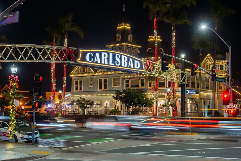Carlsbad street sign with historic building lit up at night, decorated for holidays.