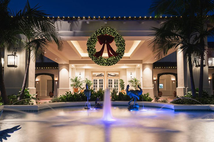 Elegant building entrance with wreath and fountain, illuminated at night.