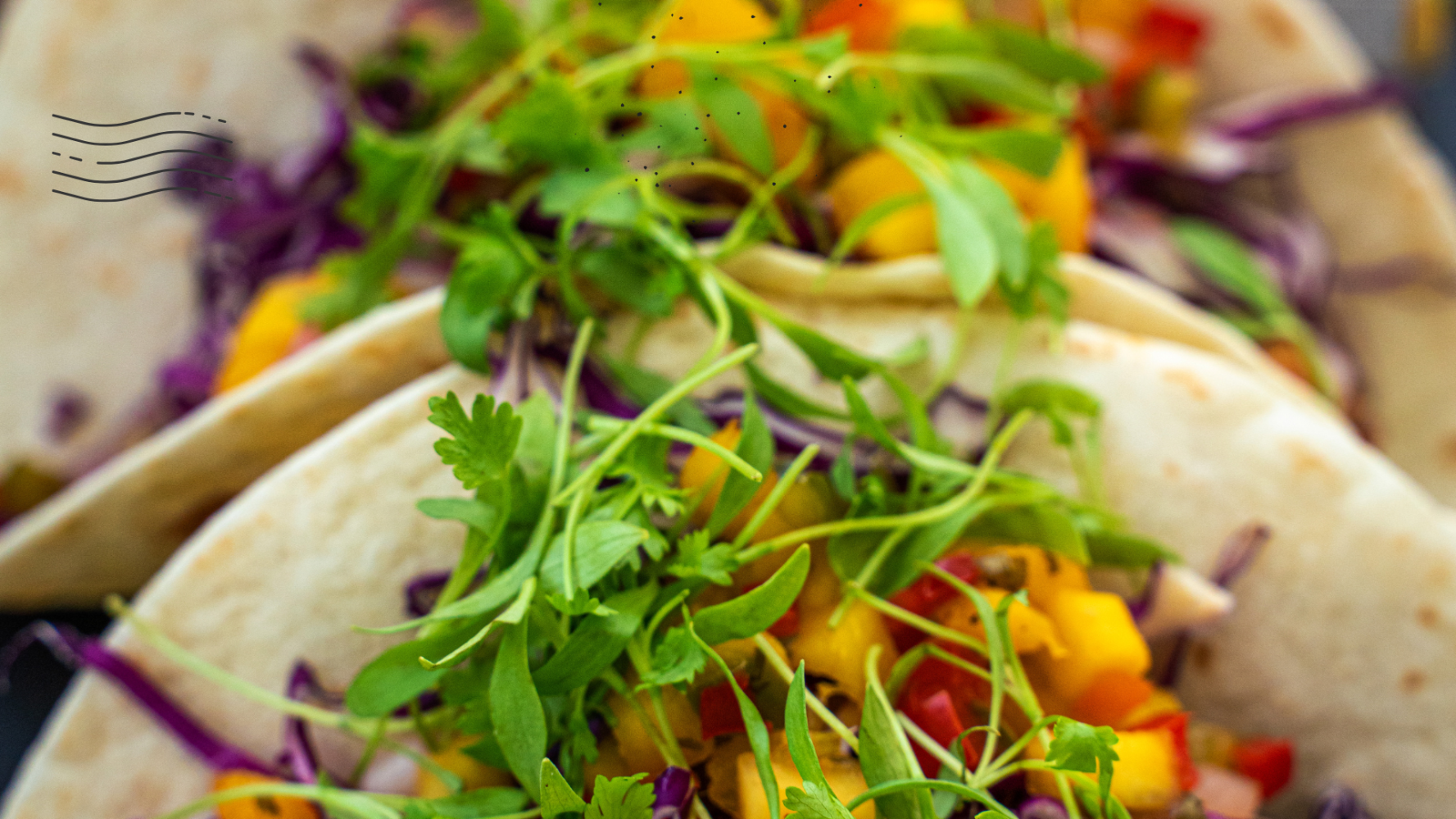Close-up of tacos with greens, mango, and purple cabbage.