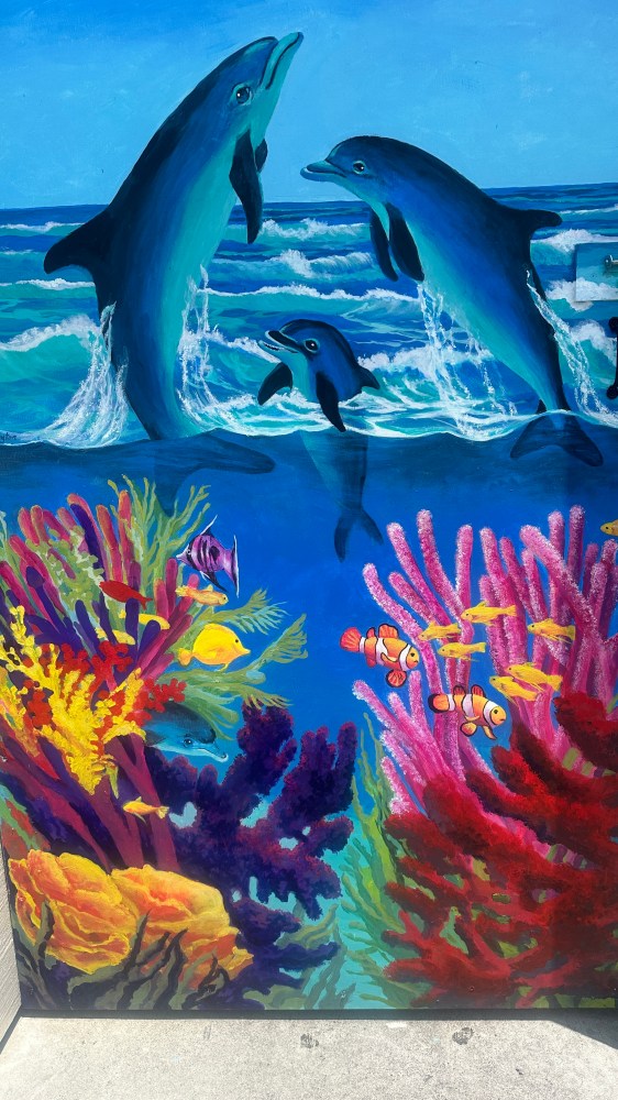 Colorful mural of dolphins leaping above waves with vibrant coral and fish below.