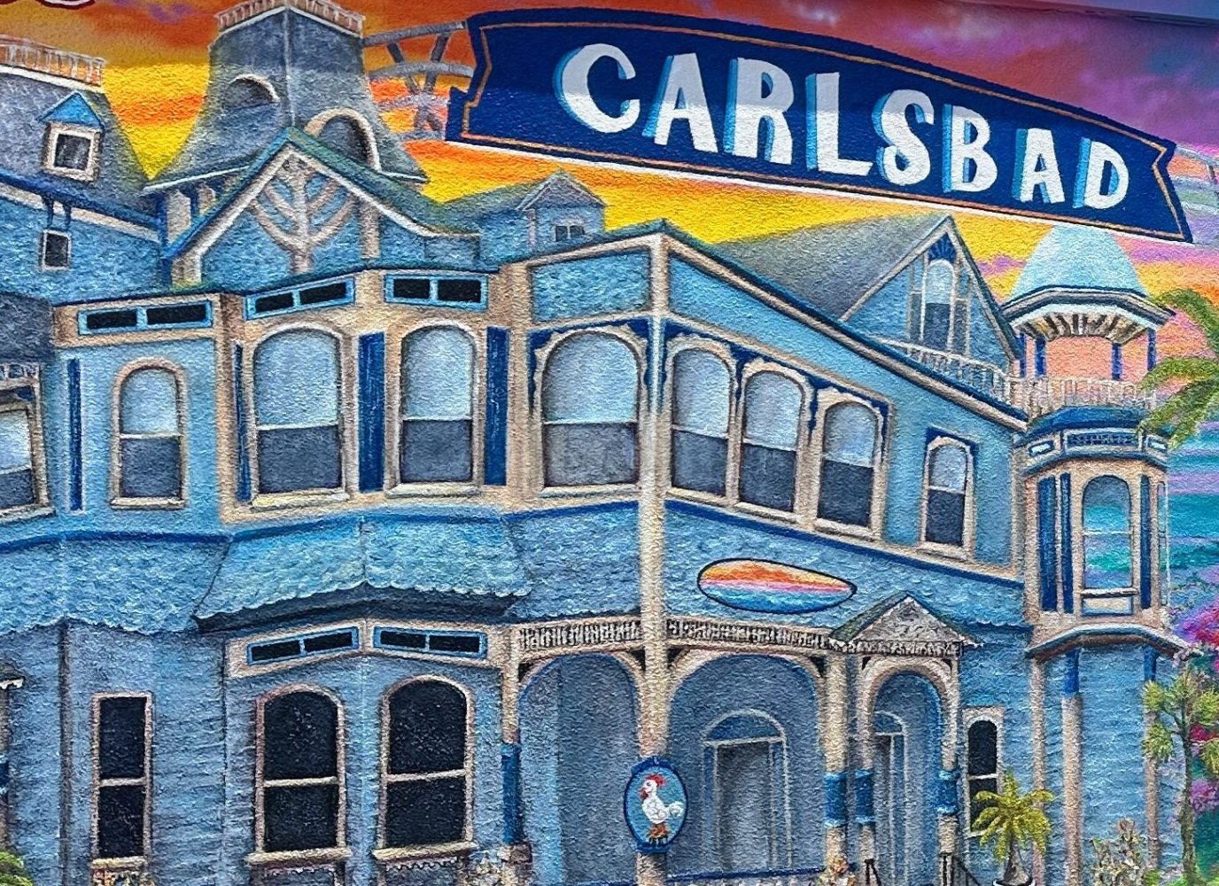 Colorful mural of a Victorian building, dolphins, coral reef, and a wave with 'Carlsbad' text.