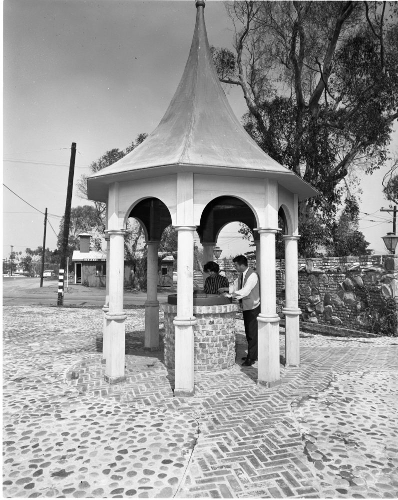 Two people standing at a small round pavilion with a peaked roof.