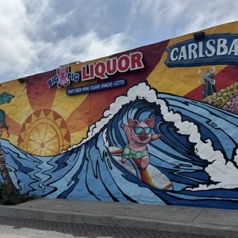 Colorful mural with pig surfing wave, 'Big Pig Liquor', and 'Carlsbad' text on building.