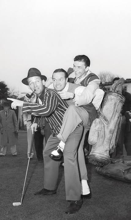 Three men on a golf course, one in a hat holding a club, another being playfully carried.