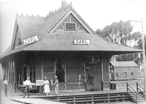 Vintage train station with people standing outside and a 'Carl' sign on top.