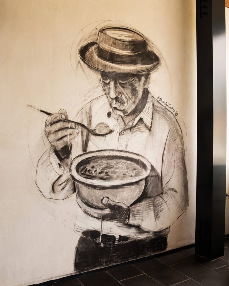 Wall art of a man in a hat eating soup from a bowl with a spoon.