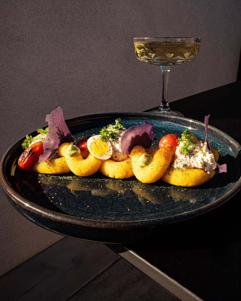 Elegant plated dish with deviled eggs, tomatoes, and herbs, plus a glass of champagne on a dark surface.