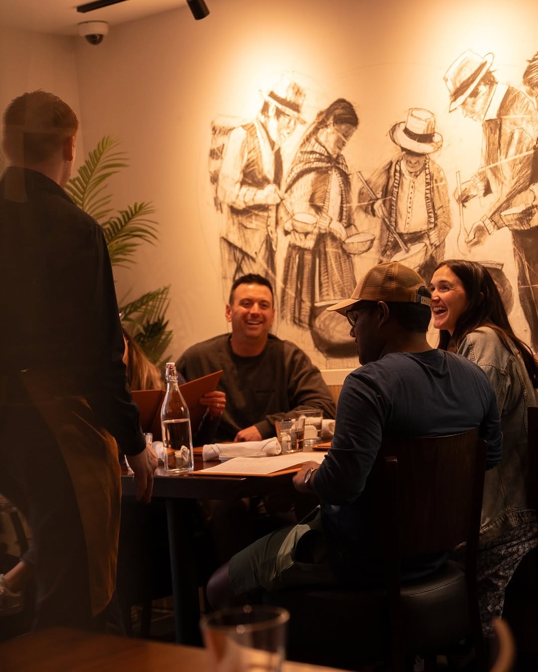 Group of people dining and laughing in a restaurant with artistic wall art.