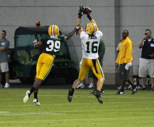 Two football players in green and white jerseys jump for a catch during practice.