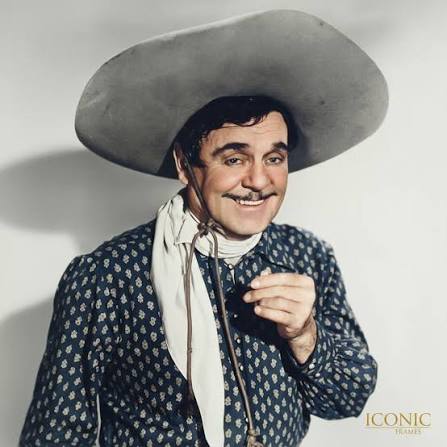 Man in patterned shirt, large hat, and neckerchief, smiling.