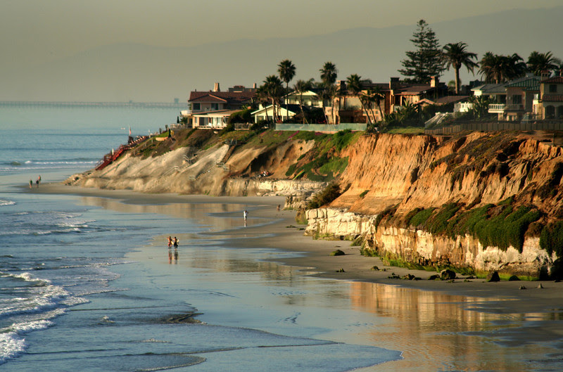 Scenic view of coastal cliffs with houses and beach at sunset.