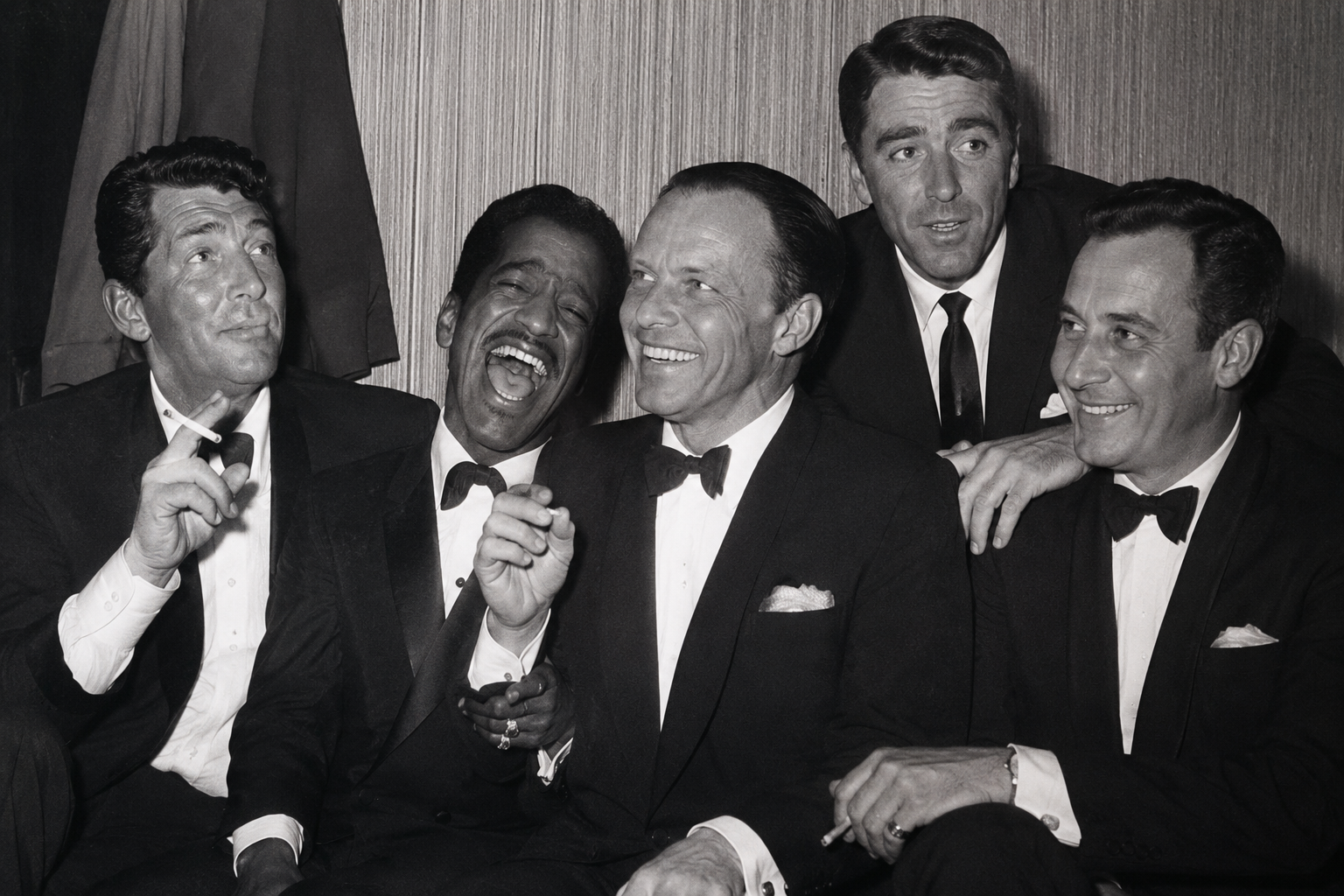 Five men in suits, smiling and laughing together in a vintage black and white photo.