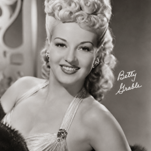 Vintage photo of a smiling woman with curled blonde hair, wearing a glamorous halter dress.