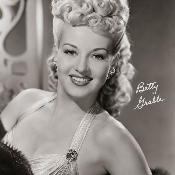 Vintage photo of a smiling woman with curled blonde hair, wearing a glamorous halter dress.