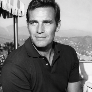 Black and white photo of a man in a polo shirt, standing outside with mountains in the background.