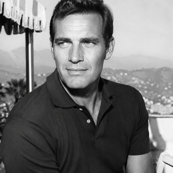 Black and white photo of a man in a polo shirt, standing outside with mountains in the background.
