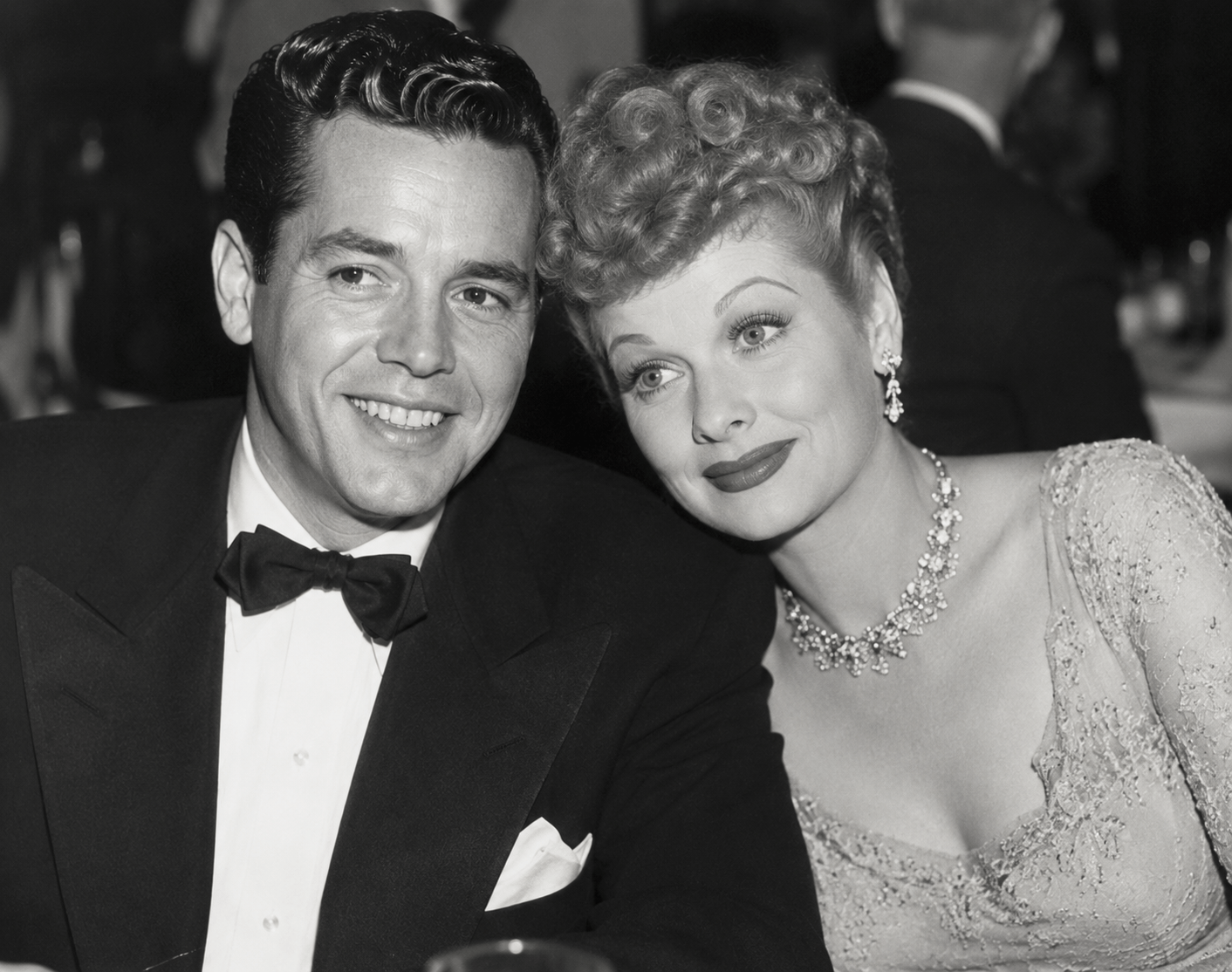 Black and white photo of a man in a tuxedo and a woman in a dress, smiling and seated closely.