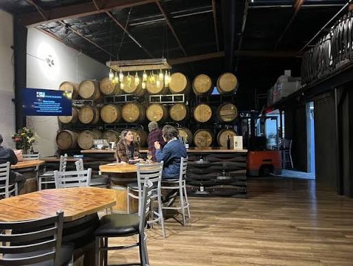People seated at tables in a brewery with barrels on the wall.