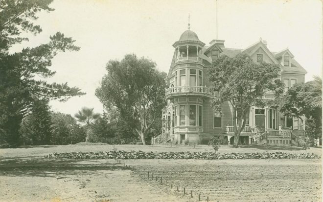 Vintage photo of a large Victorian-style house surrounded by trees.